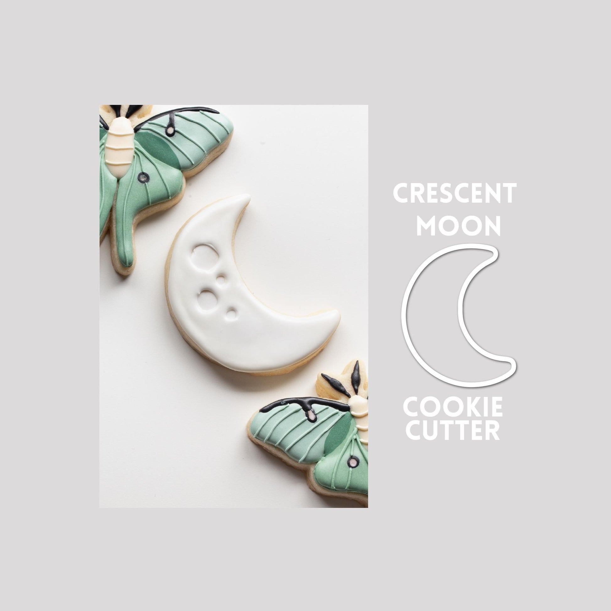 Decorated crescent moon sugar cookie next to a crescent moon cookie cutter outline on a gray background.