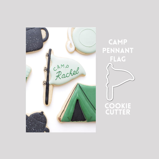 Decorated camp pennant flag sugar cookie next to a camp pennant flag cookie cutter outline on a gray background.
