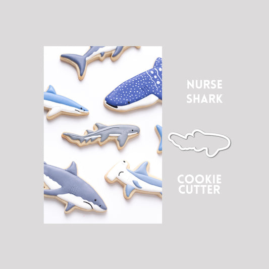 Decorated nurse shark sugar cookie next to a nurse shark cookie cutter outline on a gray background.