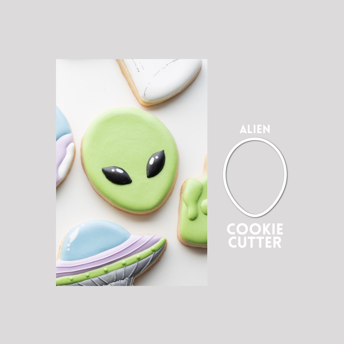 Decorated alien sugar cookie next to a alien cookie cutter outline on a gray background.