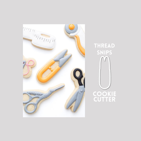 Decorated thread snips sugar cookie next to a thread snips cookie cutter outline on a gray background.