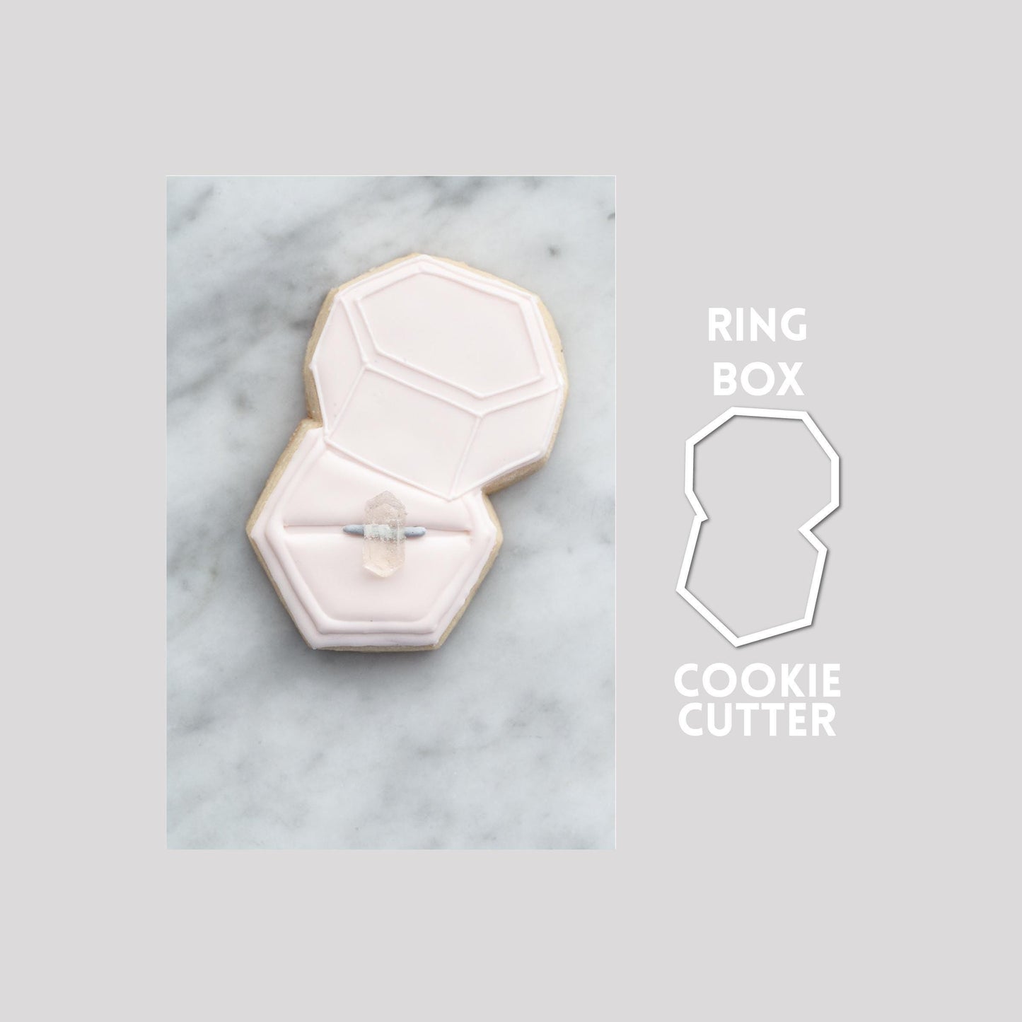 Decorated wedding box sugar cookie next to a wedding box cookie cutter outline on a gray background.