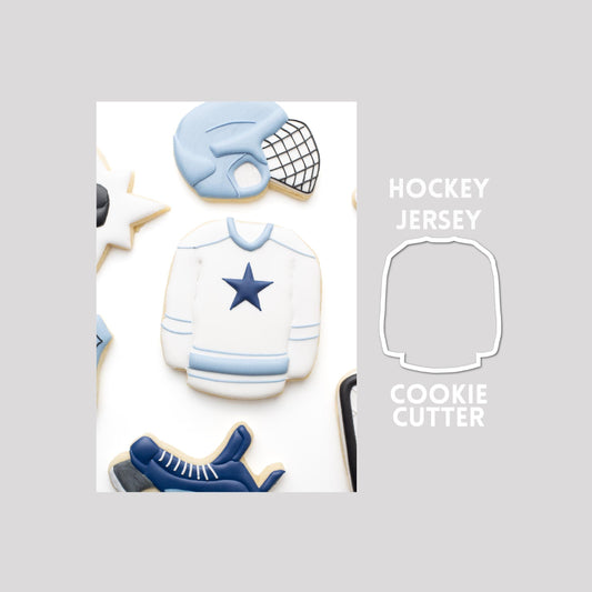 Decorated hockey jersey sugar cookie next to a hockey jersey cookie cutter outline on a gray background.