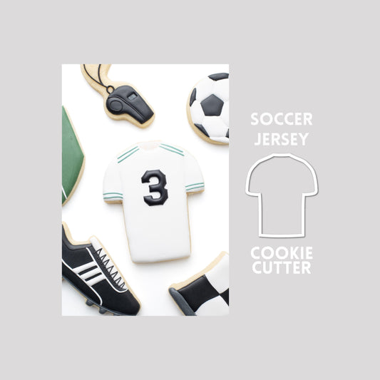 Decorated soccer jersey sugar cookie next to a soccer jersey cookie cutter outline on a gray background.