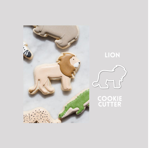 Decorated lion sugar cookie next to a lion cookie cutter outline on a gray background.