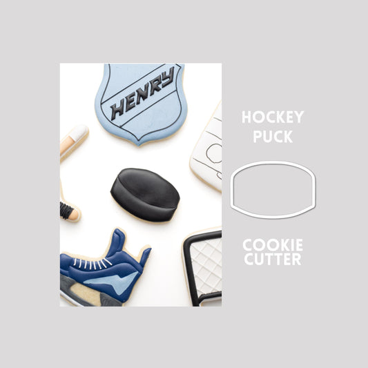Decorated hockey puck sugar cookie next to a hockey puck cookie cutter outline on a gray background.