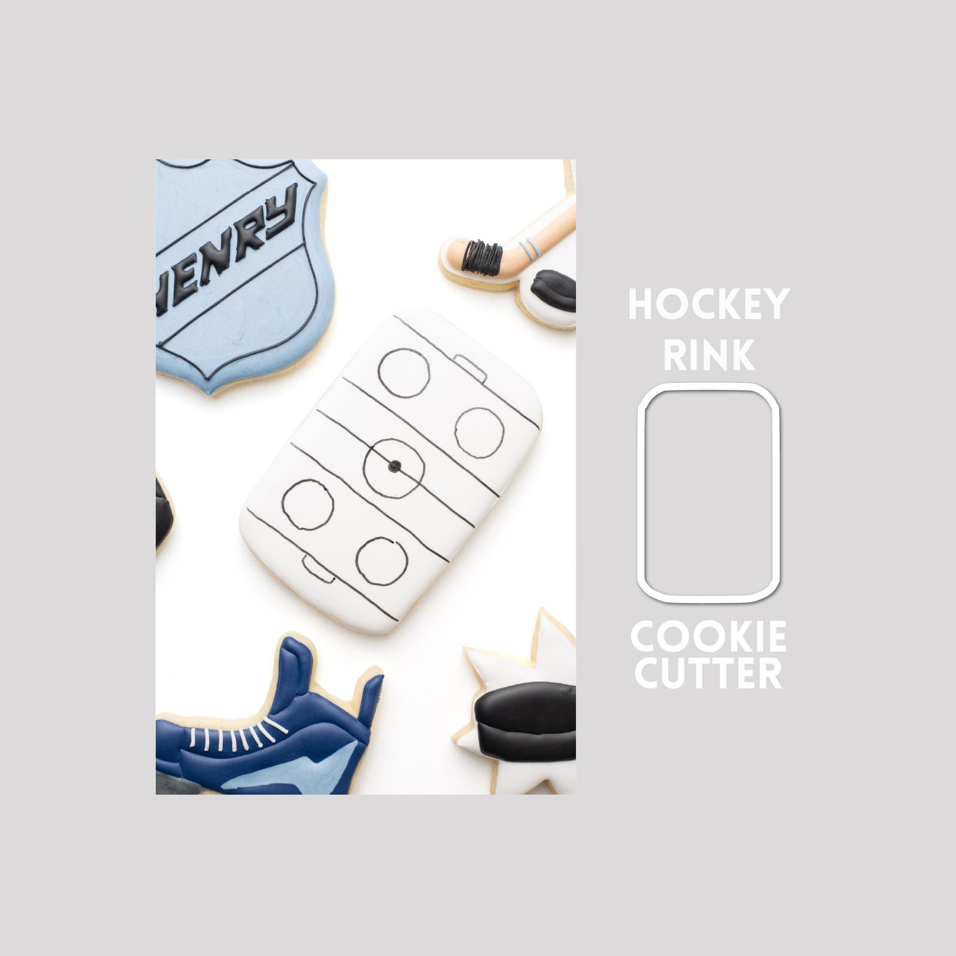 Decorated hockey rink sugar cookie next to a hockey rink cookie cutter outline on a gray background.