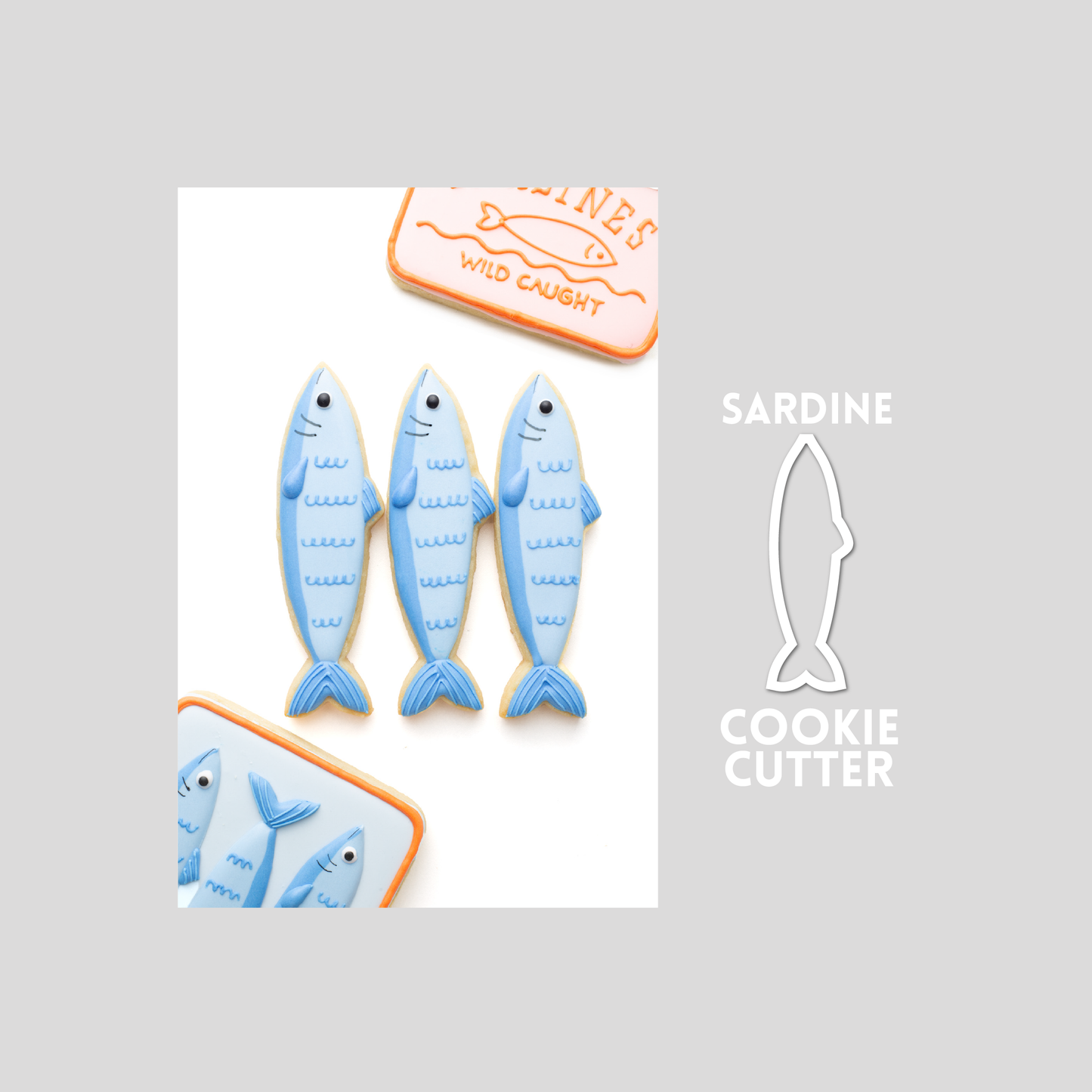Decorated sardine fish sugar cookie next to a sardine cookie cutter outline on a gray background.