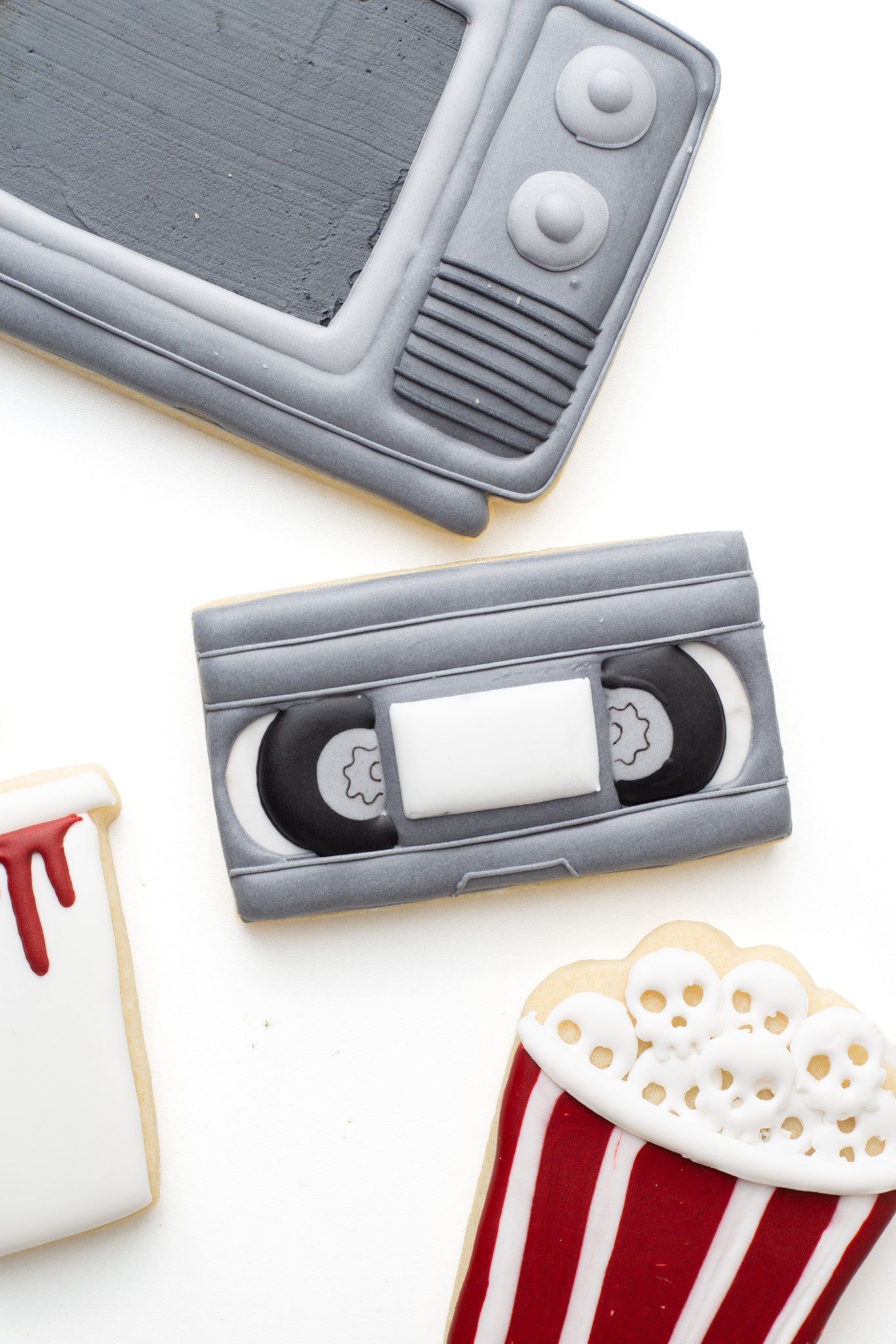 A video tape decorated sugar cookie next to a television and popcorn tub and cup with blood and skulls in a scary movie halloween theme. 
