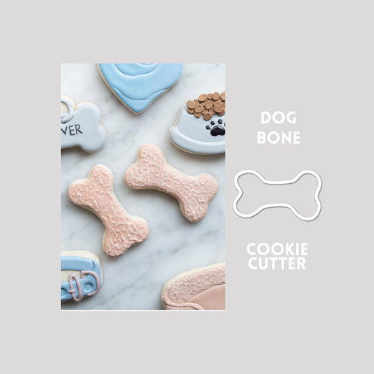 Decorated dog bone sugar cookie next to a dog bone cookie cutter outline on a gray background.