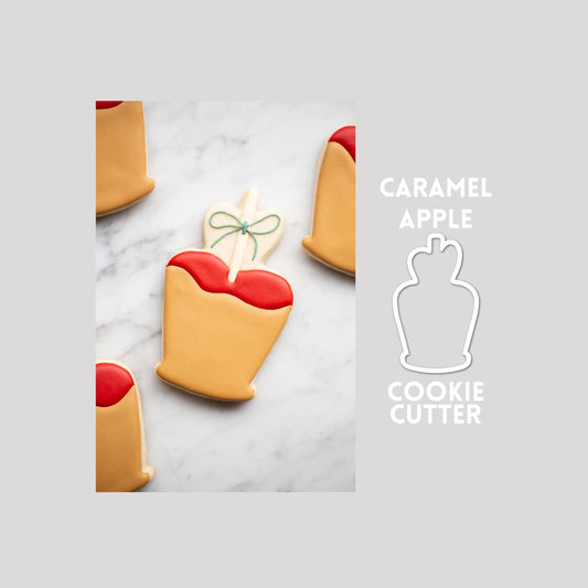 Decorated caramel apple sugar cookie next to a caramel apple cookie cutter outline on a gray background.