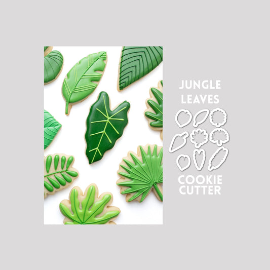 Decorated jungle leaves sugar cookies next to a jungle leaves cookie cutter outlines on a gray background.