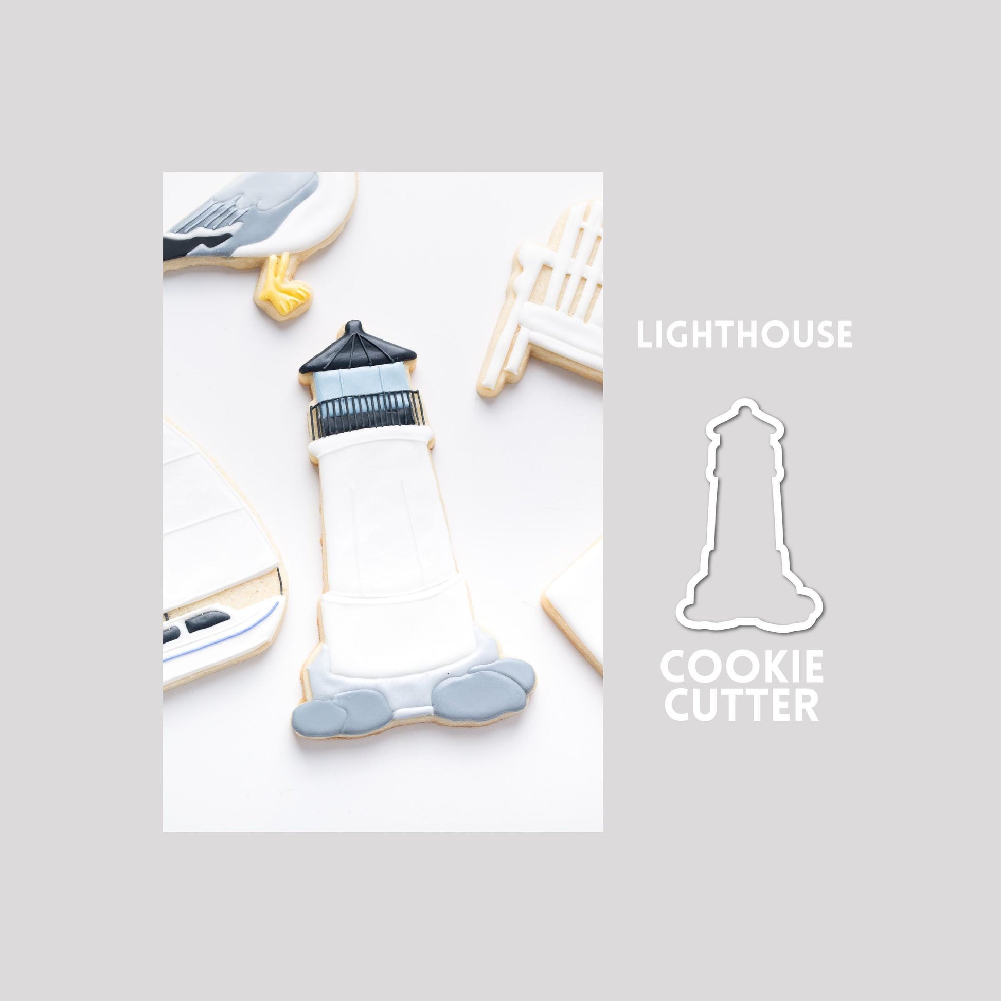 Decorated lighthouse sugar cookie next to a lighthouse cookie cutter outline on a gray background.