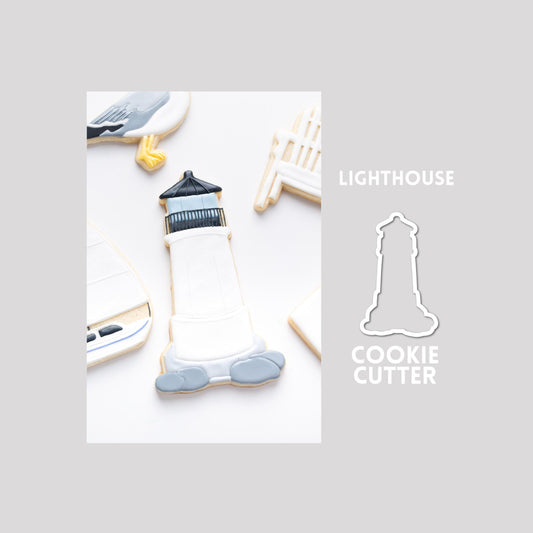 Decorated lighthouse sugar cookie next to a lighthouse cookie cutter outline on a gray background.