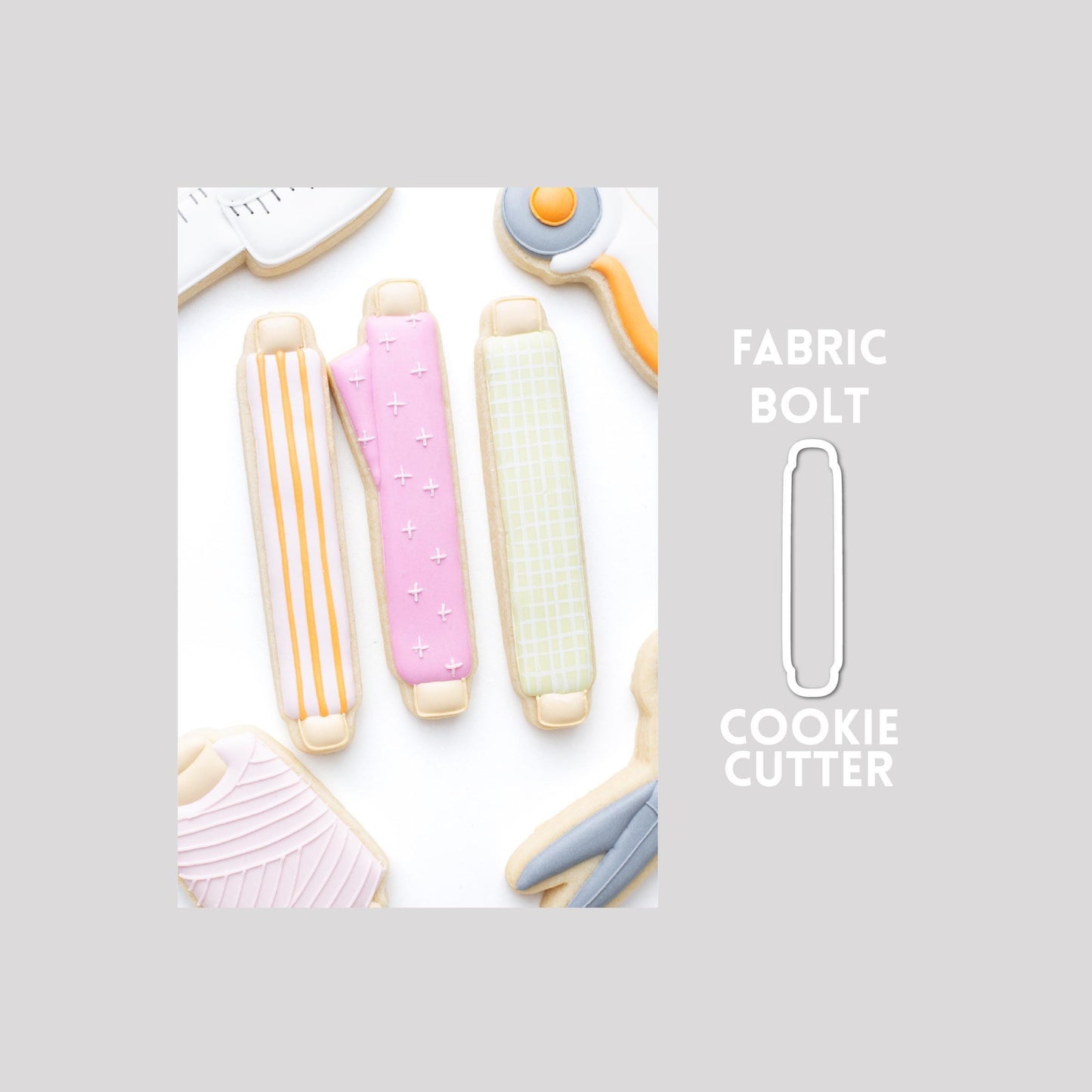 Decorated fabric bolt sugar cookie next to a fabric bolt cookie cutter outline on a gray background.