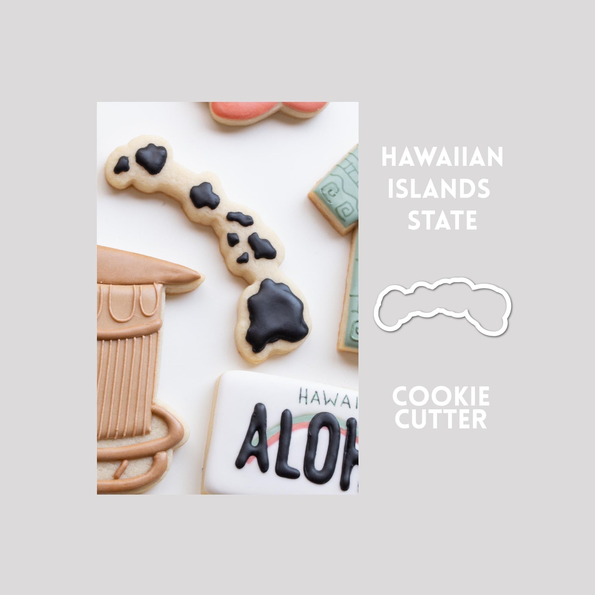 Decorated state of Hawaii sugar cookie next to a state of Hawaii cookie cutter outline on a gray background.