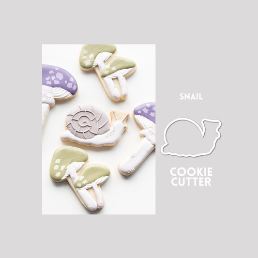 Decorated snail sugar cookie next to a snail cookie cutter outline on a gray background.