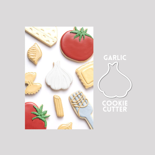 Decorated garlic sugar cookie next to a garlic cookie cutter outline on a gray background.