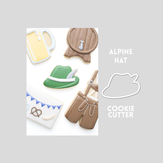 Decorated Alpine Hat sugar cookie next to a Alpine Hat cookie cutter outline on a gray background.