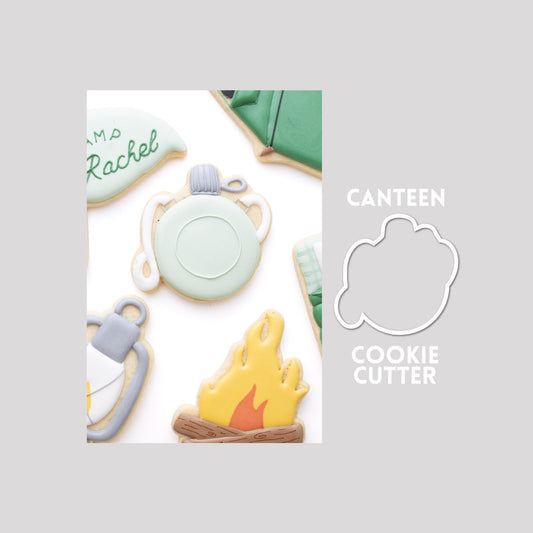 Decorated canteen sugar cookie next to a canteen cookie cutter outline on a gray background.