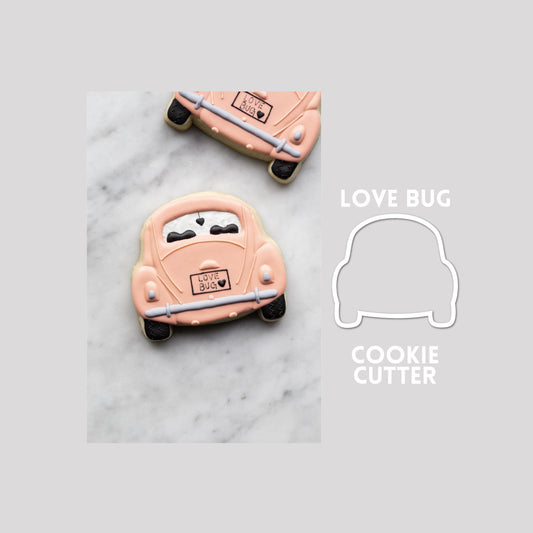 Decorated love bug sugar cookie next to a love bug cookie cutter outline on a gray background.