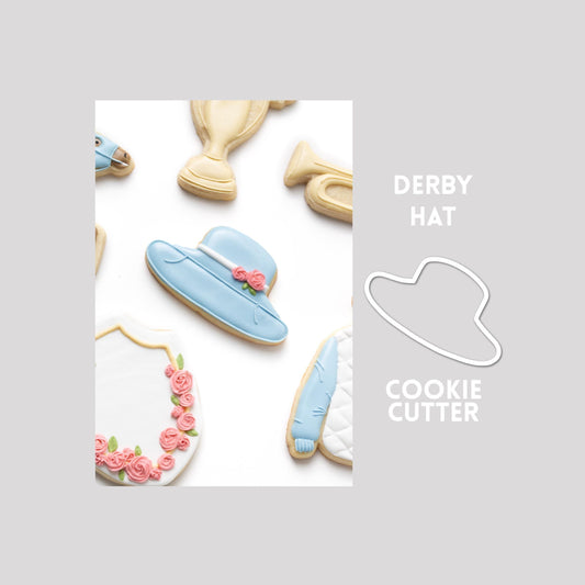 Decorated derby hat sugar cookie next to a derby hat cookie cutter outline on a gray background.