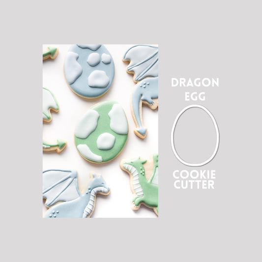 Decorated dragon egg sugar cookie next to a dragon egg cookie cutter outline on a gray background.