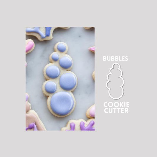 Decorated bubbles sugar cookie next to a bubbles cookie cutter outline on a gray background.