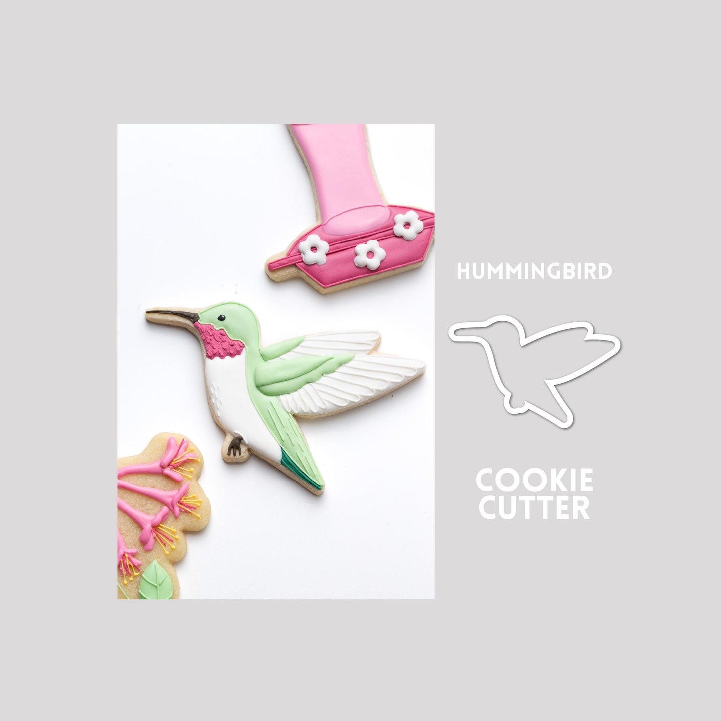 Decorated hummingbird sugar cookie next to a hummingbird cookie cutter outline on a gray background.