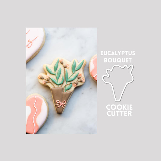 Decorated eucalyptus bouquet sugar cookie next to a eucalyptus bouquet cookie cutter outline on a gray background.