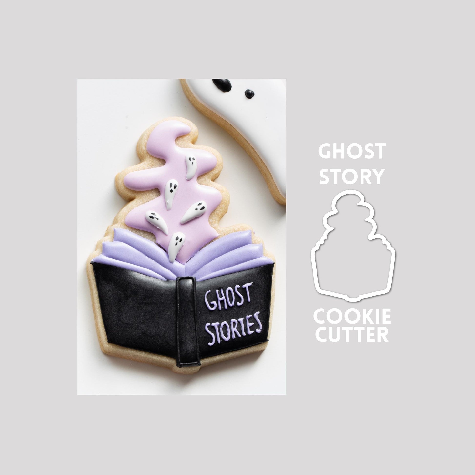 Decorated ghost story book sugar cookie next to a ghost story book cookie cutter outline on a gray background.
