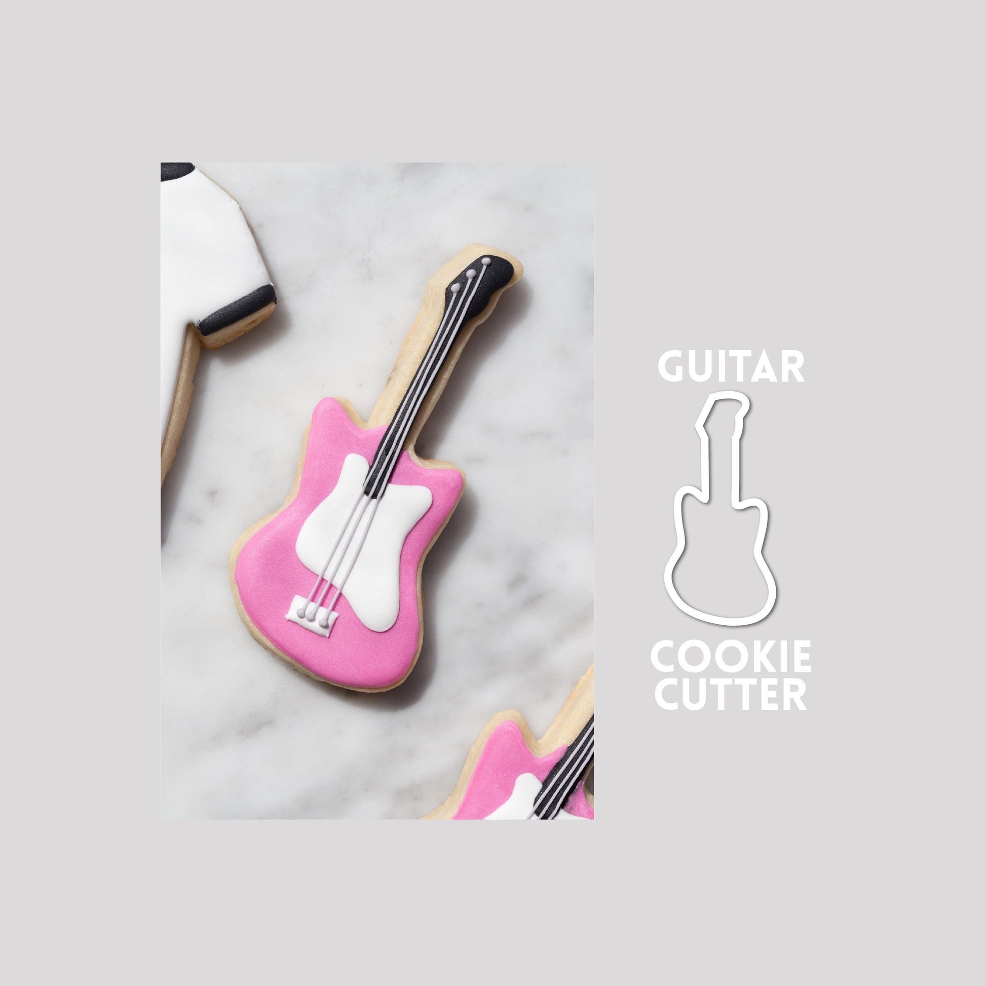 Decorated guitar sugar cookie next to a guitar cookie cutter outline on a gray background.