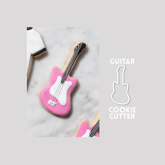 Decorated guitar sugar cookie next to a guitar cookie cutter outline on a gray background.