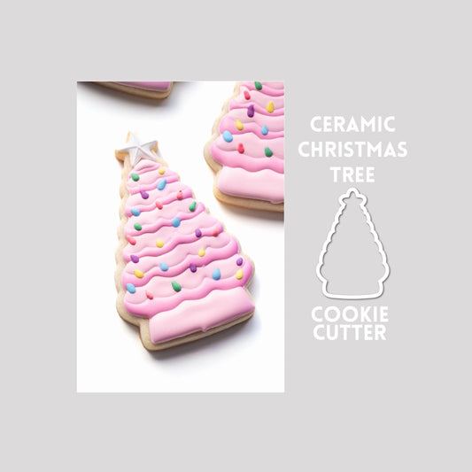 Decorated ceramic christmas tree sugar cookie next to a ceramic christmas tree cookie cutter outline on a gray background.