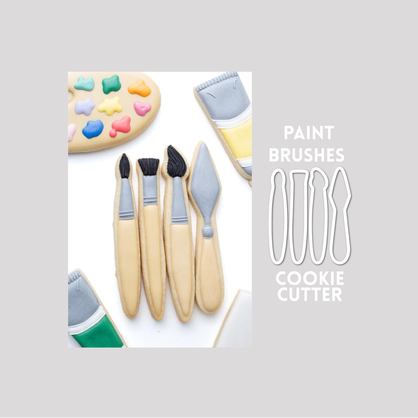 Decorated paint brushes sugar cookie next to a paint brushes cookie cutter outline on a gray background.