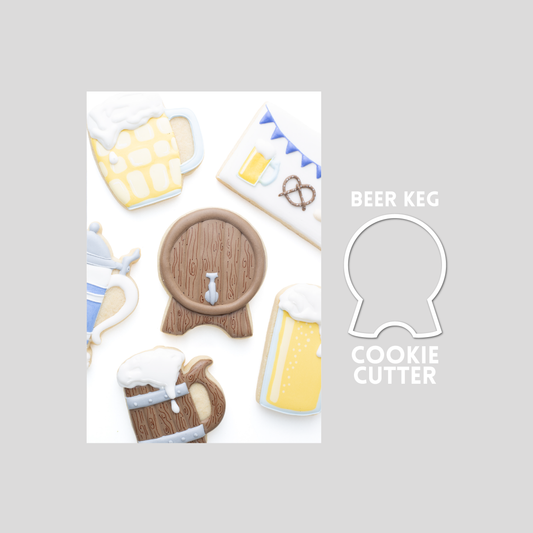 Decorated beer keg sugar cookie next to a beer keg cookie cutter outline on a gray background.