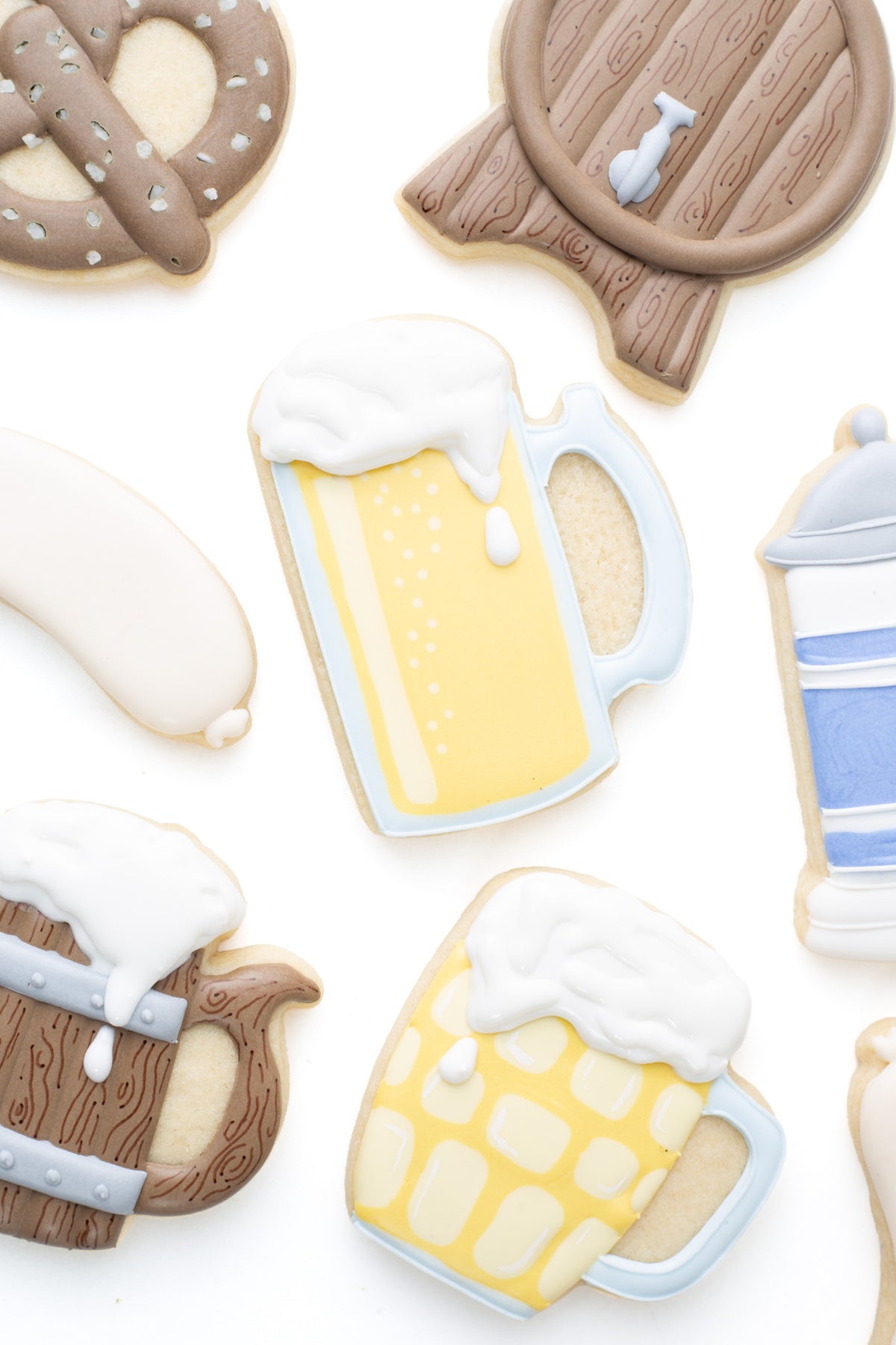Oktoberfest themed cookies. A beer mug decorated sugar cookie next to a ,  beer stein, wood beer mug, keg, pretzel and bratwurst decorated sugar cookie.