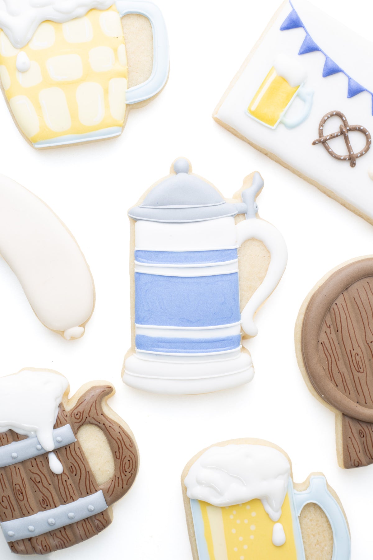 A beer stein decorated sugar cookie next to a wood beer stein, beer mug, keg,  and bratwurst decorated sugar cookie.