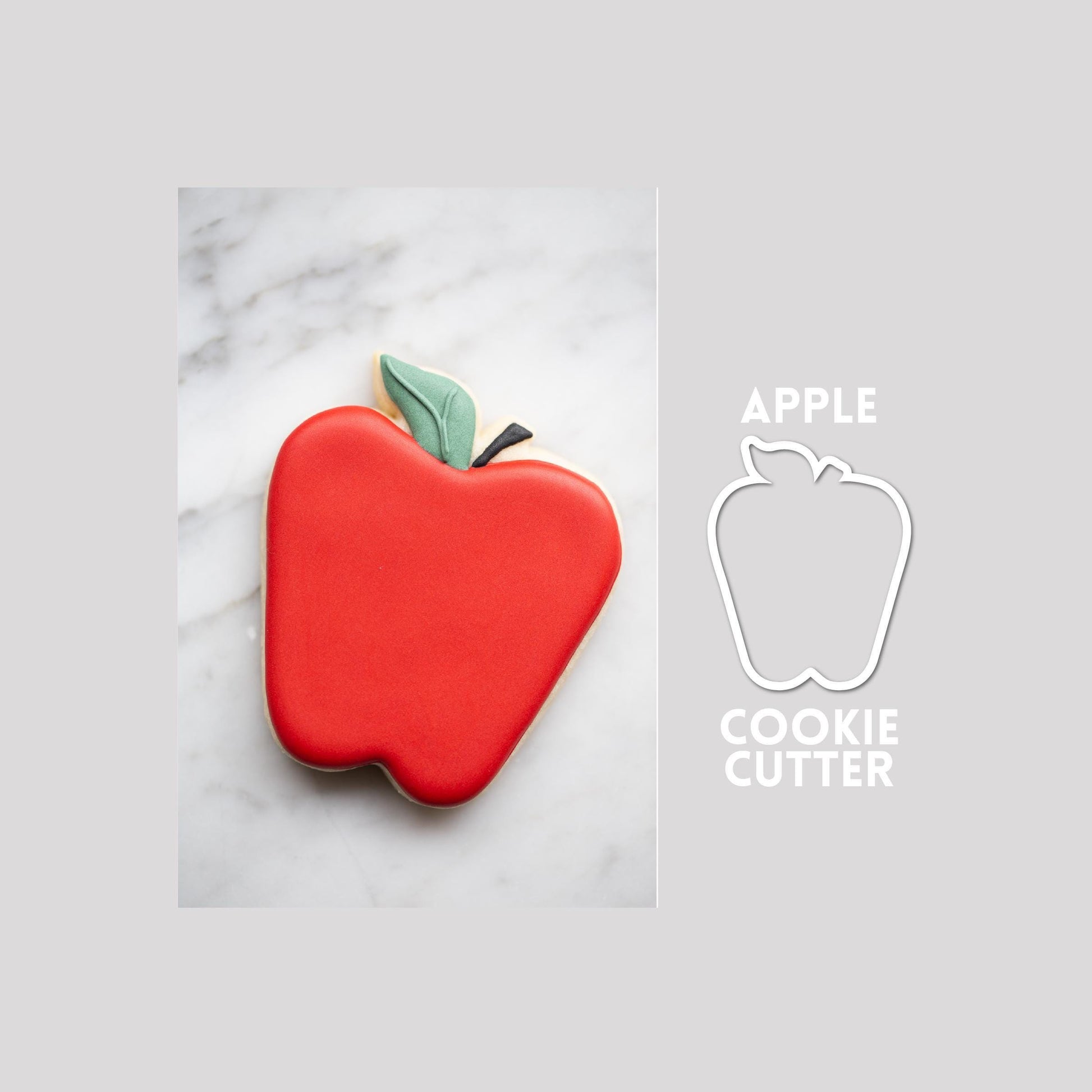 Decorated apple sugar cookie next to a apple cookie cutter outline on a gray background.