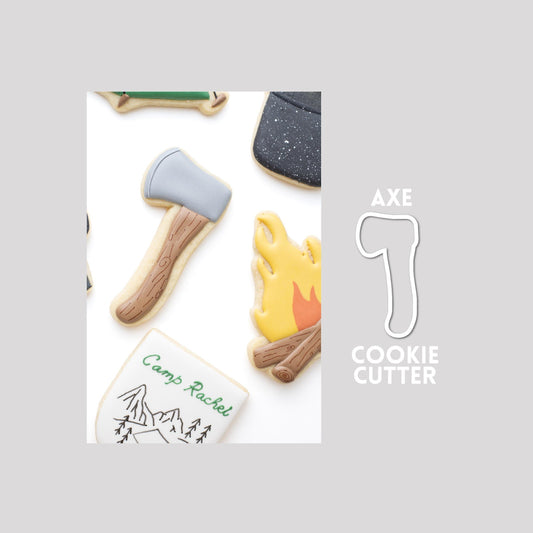 Decorated axe sugar cookie next to a axe cookie cutter outline on a gray background.