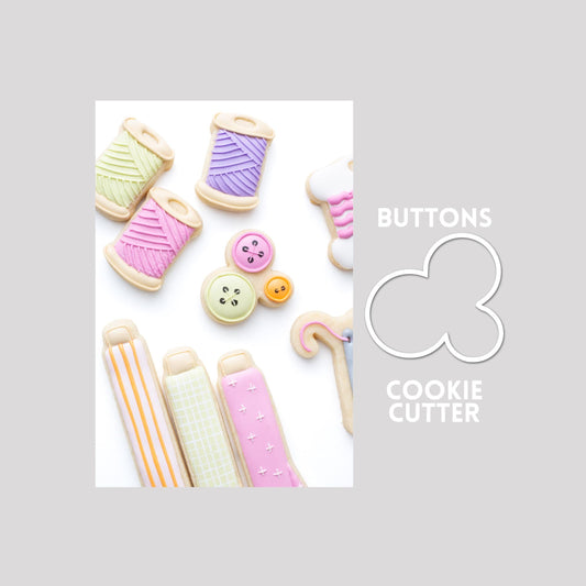 Decorated buttons sugar cookie next to a buttons cookie cutter outline on a gray background.