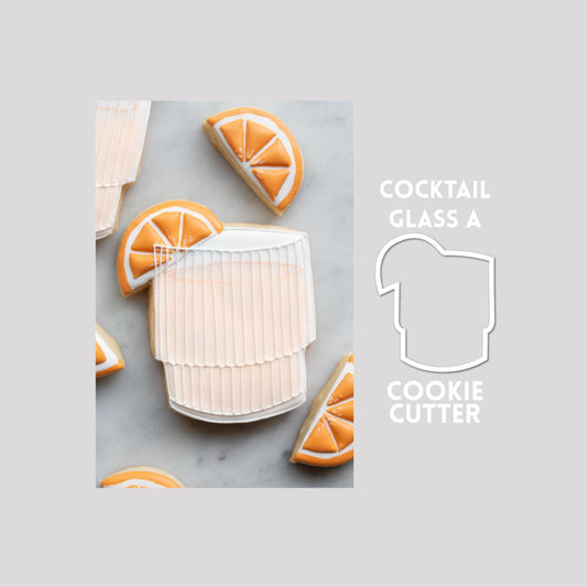 Decorated cocktail glass sugar cookie next to a cocktail glass cookie cutter outline on a gray background.