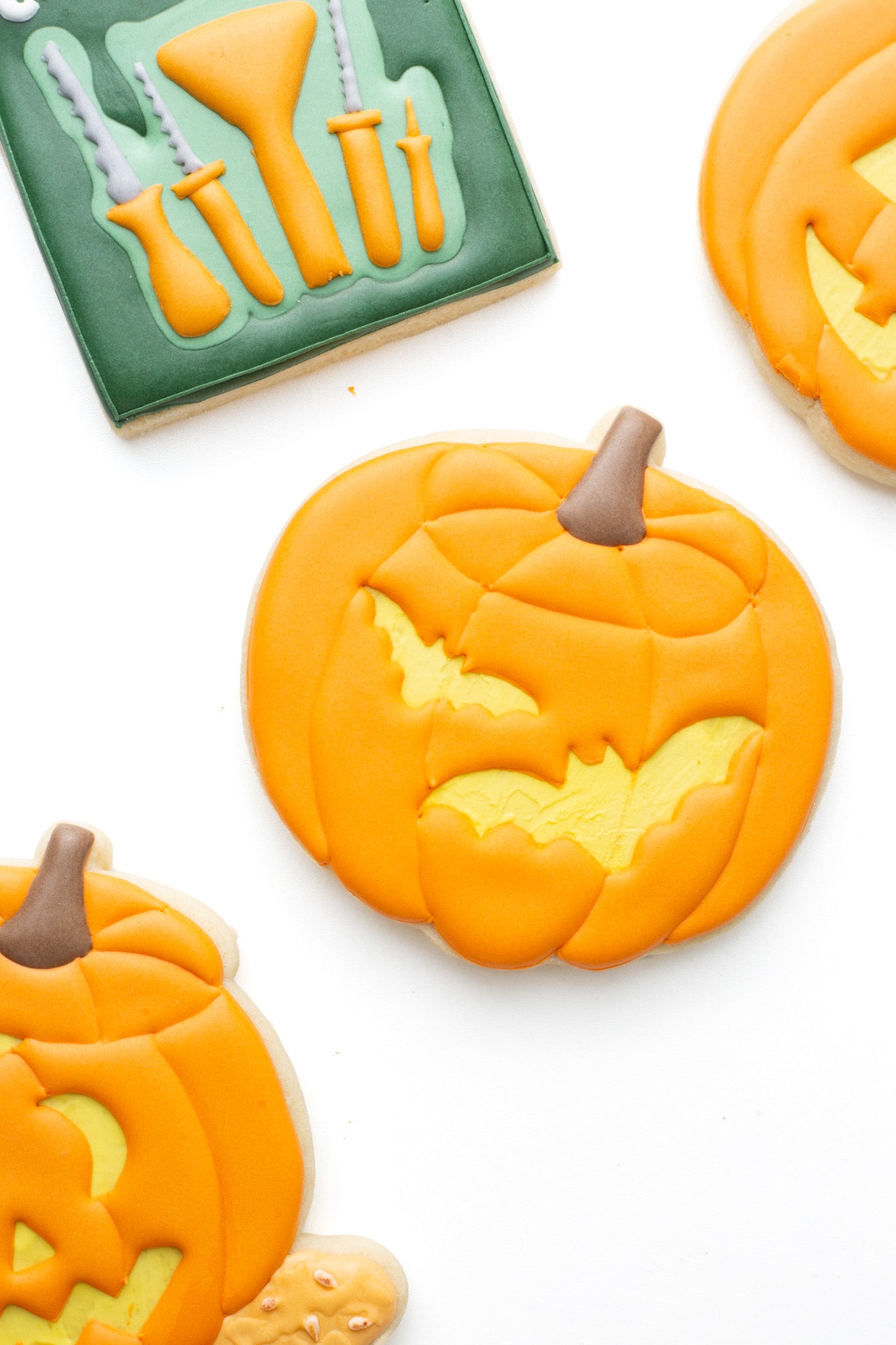 Carved pumpkin with bats decorated sugar cookie next to other carved pumpkins and pumpkin carving tools.