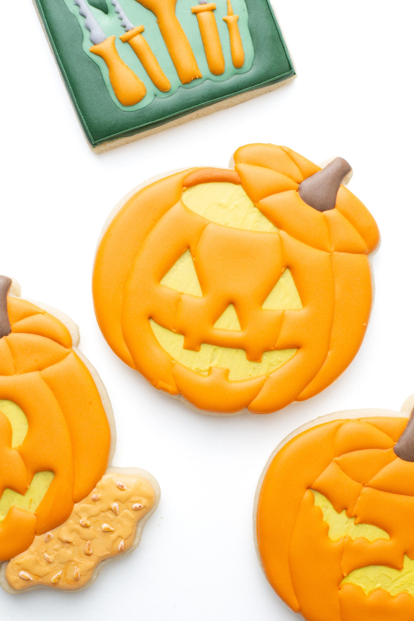 Carved pumpkin decorated sugar cookie next to other carved pumpkins and pumpkin carving tools.