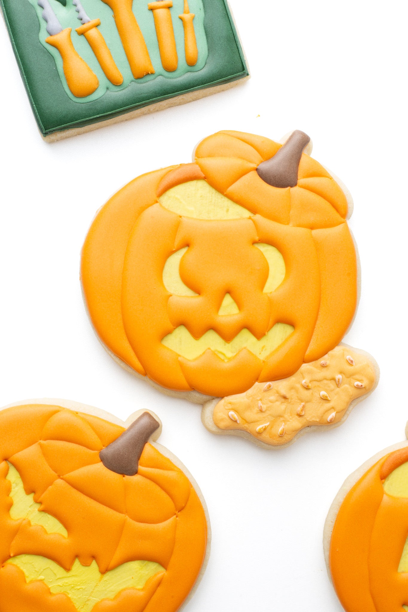 Carved pumpkin with seeds and guts decorated sugar cookie next to other carved pumpkins and pumpkin carving tools.