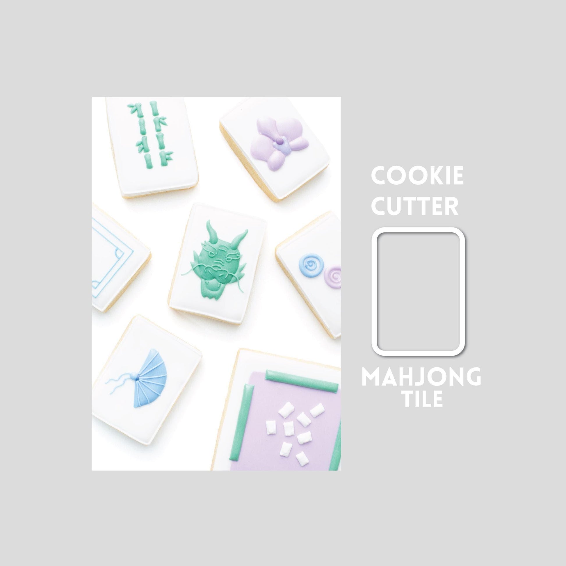 Decorated mahjong tile sugar cookie next to a mahjong tile cookie cutter outline on a gray background.