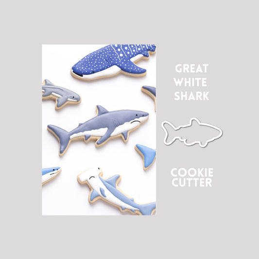 Decorated great white shark sugar cookie next to a great white shark cookie cutter outline on a gray background.