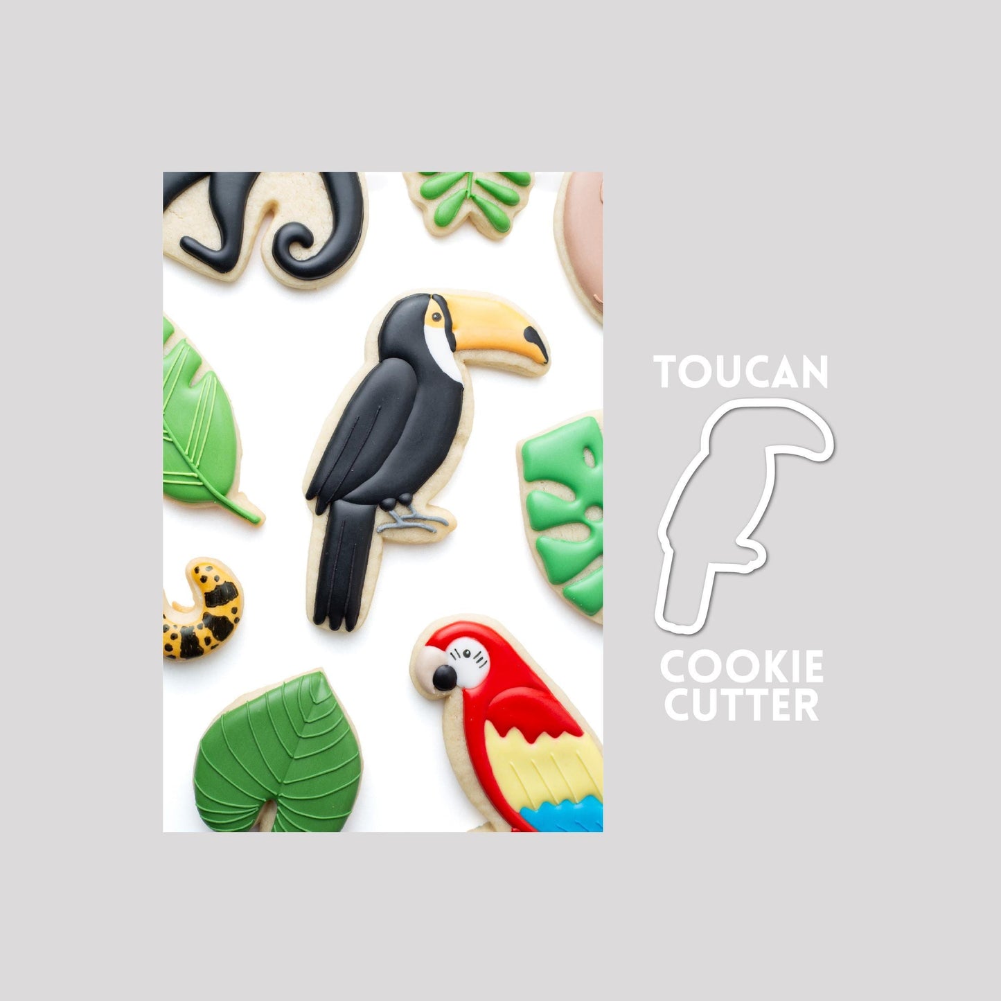 Decorated toucan sugar cookie next to a toucan cookie cutter outline on a gray background.