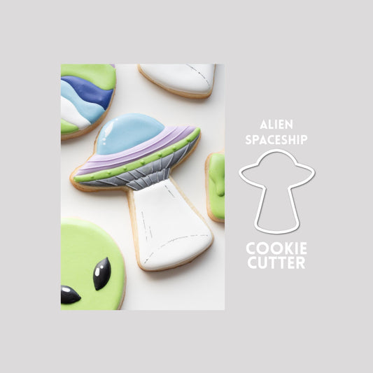 Decorated alien spaceship sugar cookie next to a alien spaceship cookie cutter outline on a gray background.