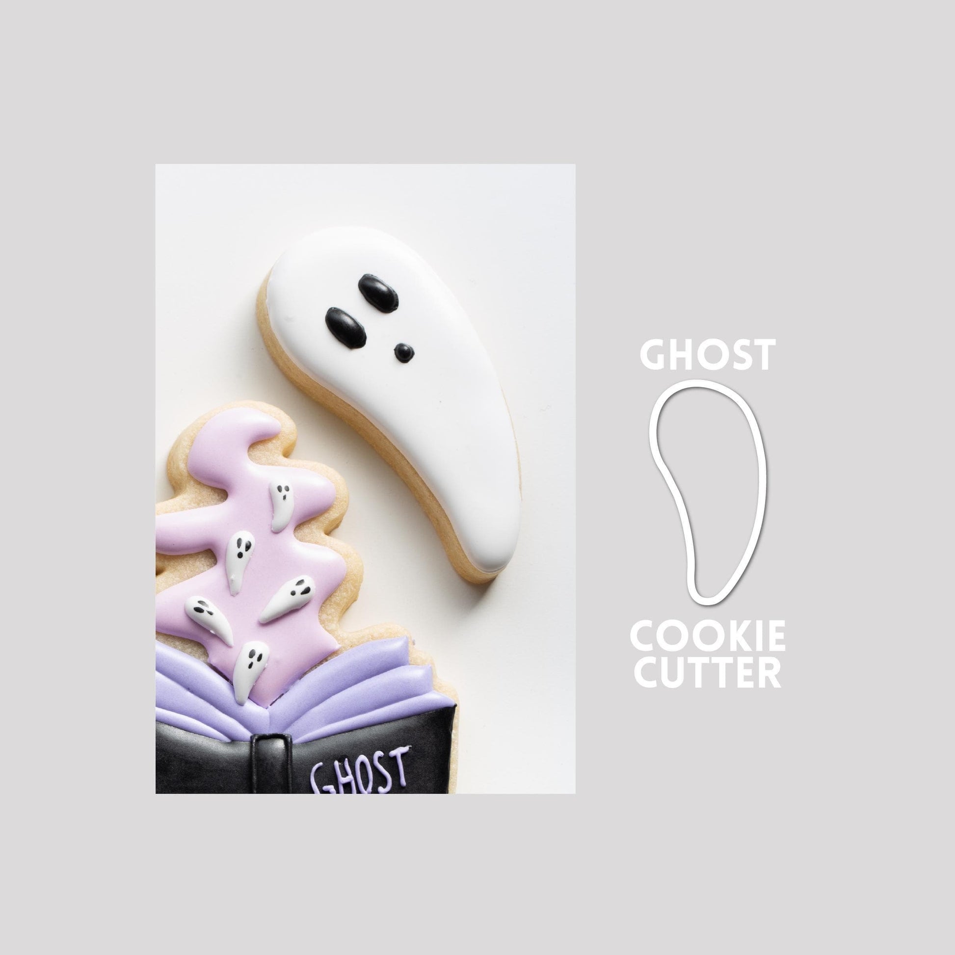 Decorated ghost sugar cookie next to a ghost cookie cutter outline on a gray background.